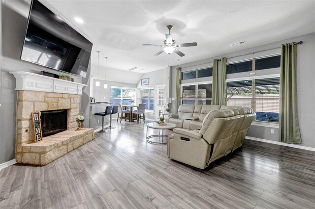 living area with vaulted ceiling, visible vents, a stone fireplace, baseboards, and ceiling fan