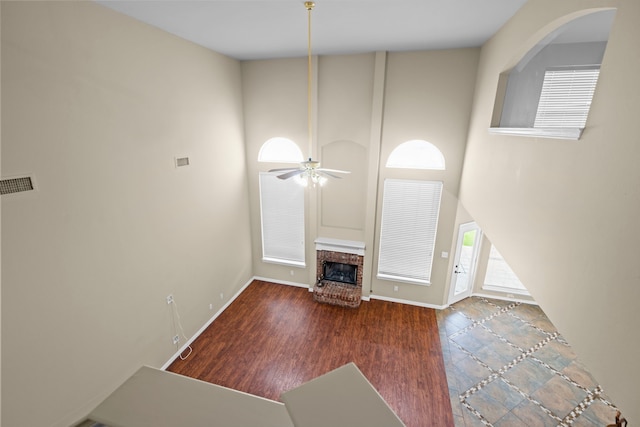 unfurnished living room with baseboards, visible vents, a high ceiling, ceiling fan, and a fireplace