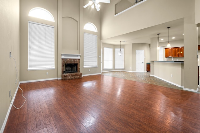 unfurnished living room with a towering ceiling, dark wood-style floors, a ceiling fan, baseboards, and a fireplace