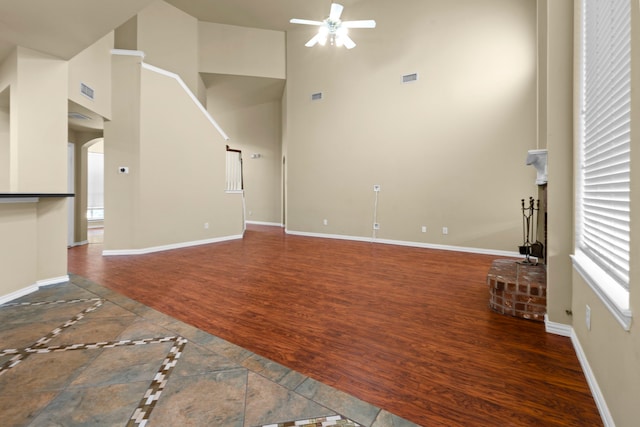 unfurnished living room with arched walkways, a towering ceiling, visible vents, a ceiling fan, and wood finished floors