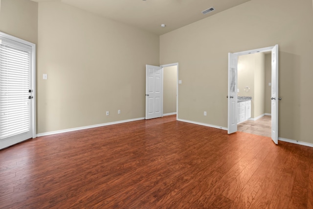 unfurnished bedroom featuring baseboards, wood finished floors, visible vents, and a high ceiling