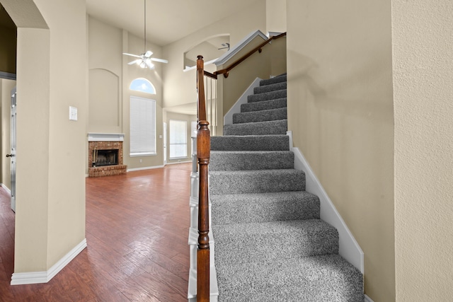 staircase featuring wood finished floors, a towering ceiling, baseboards, and ceiling fan