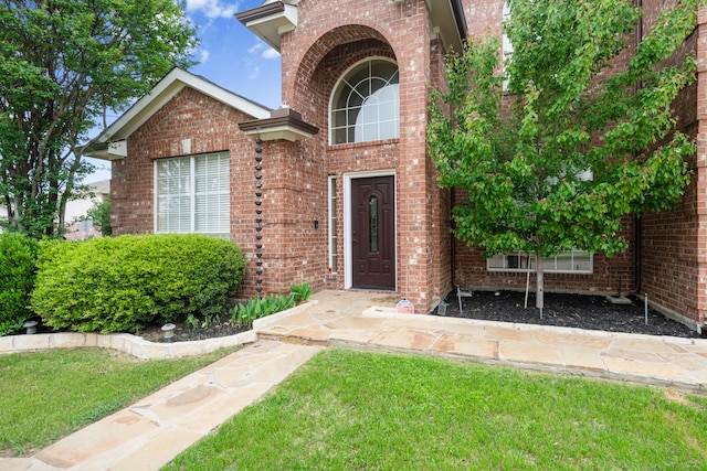 view of exterior entry featuring brick siding and a yard