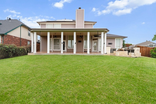 back of property featuring a chimney, a ceiling fan, a yard, roof mounted solar panels, and a patio