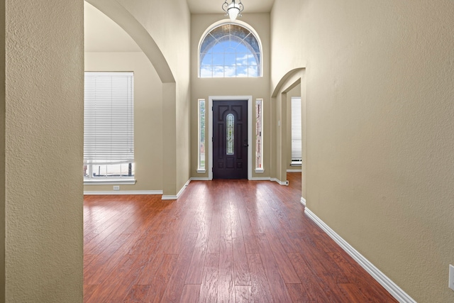 entrance foyer with arched walkways, a textured wall, baseboards, and dark wood-style flooring