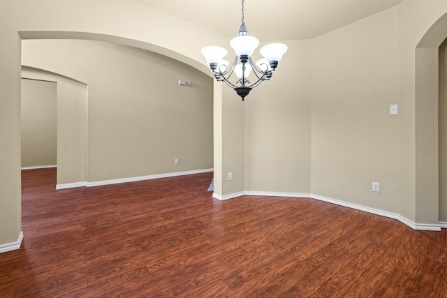 empty room featuring baseboards, wood finished floors, arched walkways, and a notable chandelier