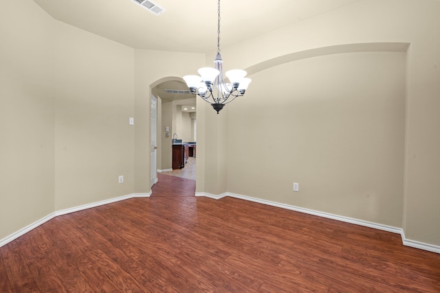 spare room featuring arched walkways, an inviting chandelier, dark wood finished floors, baseboards, and visible vents