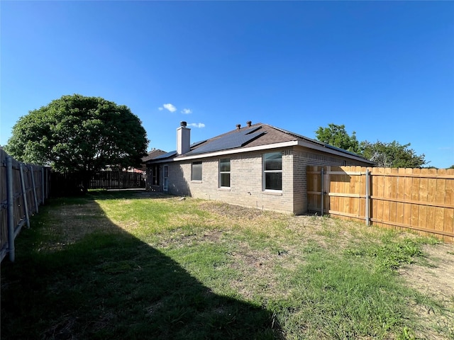 525 Reagan Ln, Burleson, TX 76028 - rear view of property featuring a chimney, a lawn, a fenced backyard, solar panels, and brick siding