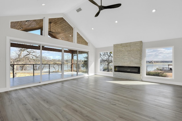 unfurnished living room with a water view, a ceiling fan, baseboards, a fireplace, and high vaulted ceiling