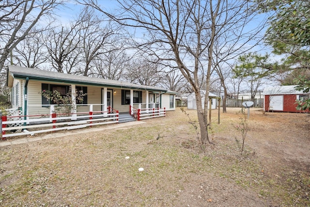 view of front facade featuring fence, an outbuilding, covered porch, and a shed