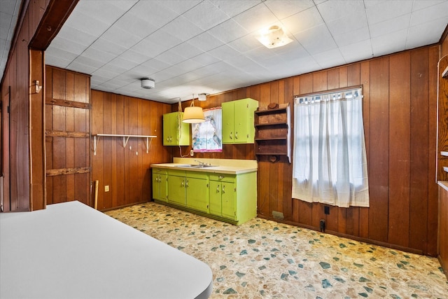 kitchen with green cabinetry, light countertops, wooden walls, a sink, and baseboards