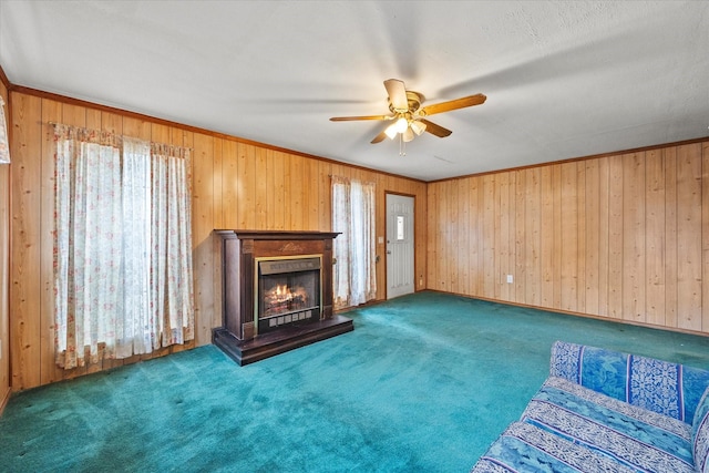 unfurnished living room with carpet, ceiling fan, a lit fireplace, baseboards, and wood walls