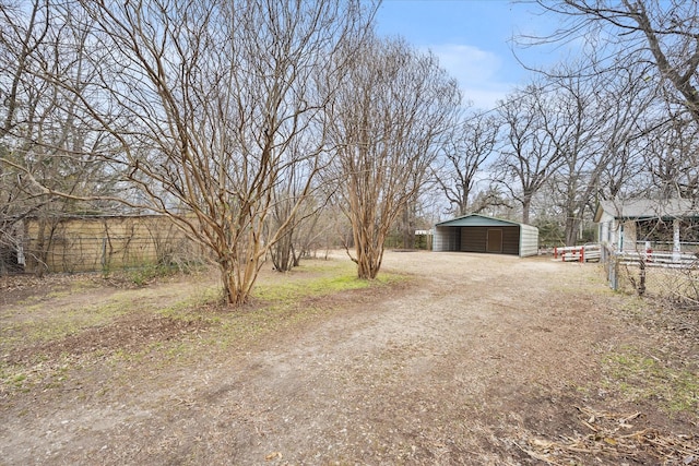 view of yard featuring an outdoor structure, dirt driveway, a detached carport, and fence