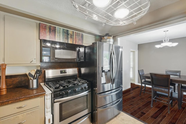 kitchen with an inviting chandelier, appliances with stainless steel finishes, wood finished floors, and dark countertops