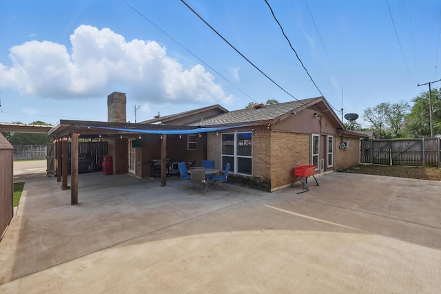 rear view of property with fence, a patio, a chimney, and brick siding
