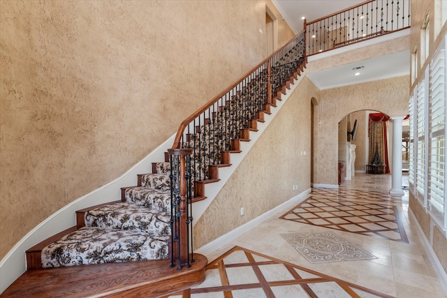 stairway with arched walkways, decorative columns, baseboards, a high ceiling, and crown molding