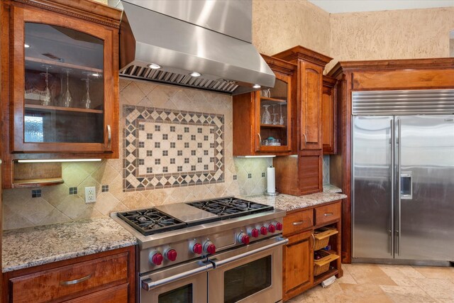 kitchen featuring brown cabinetry, range hood, high quality appliances, and light stone counters