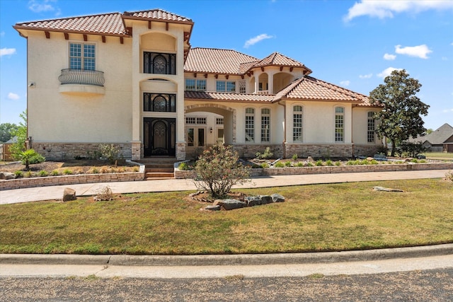 mediterranean / spanish-style home featuring stone siding, a tiled roof, a front lawn, and stucco siding