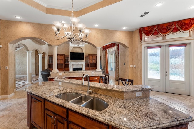 kitchen with a sink, arched walkways, open floor plan, decorative columns, and an island with sink