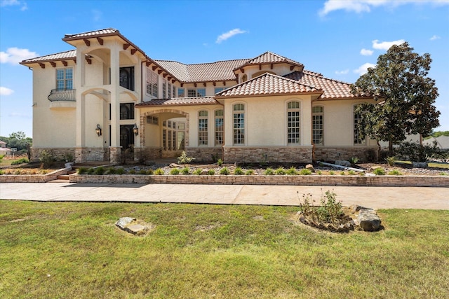 mediterranean / spanish home with stone siding, a tiled roof, a front yard, and stucco siding