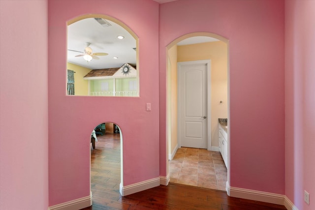 corridor with baseboards, wood finished floors, visible vents, and arched walkways