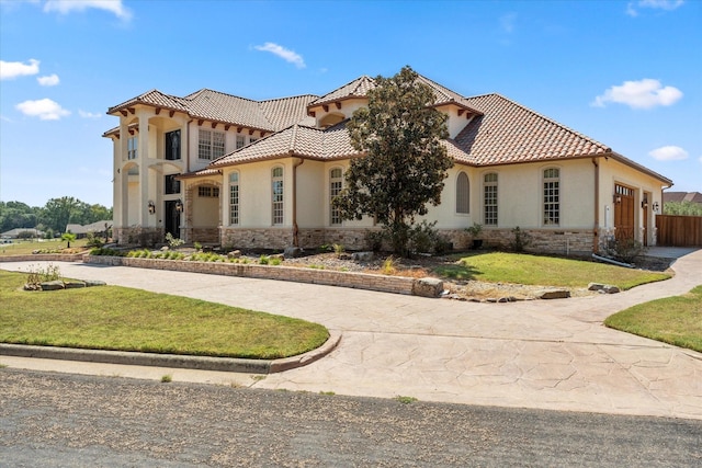 mediterranean / spanish-style house featuring a front lawn, stone siding, a tiled roof, and curved driveway