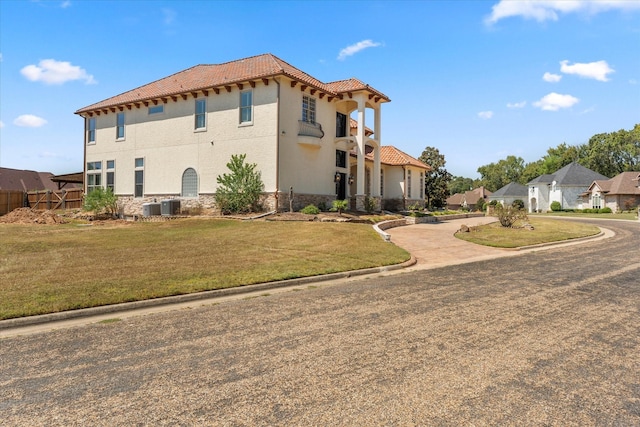 view of side of home with central AC, stone siding, a tiled roof, a yard, and stucco siding