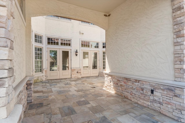 entrance to property featuring stucco siding, stone siding, and french doors