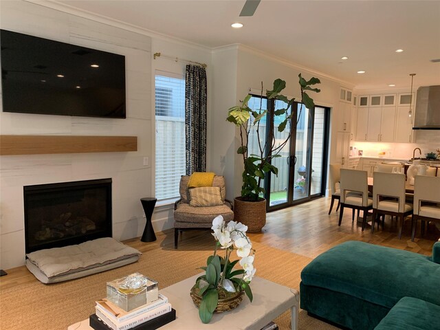 living room with ornamental molding, plenty of natural light, light wood-style flooring, recessed lighting, and a fireplace