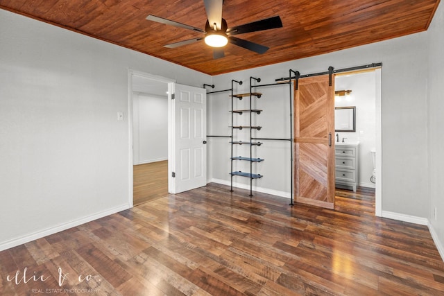 unfurnished bedroom featuring a barn door, wood finished floors, baseboards, wood ceiling, and ensuite bathroom
