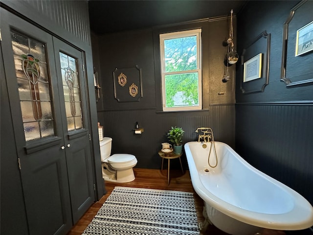 501 N Austin St, Comanche, TX 76442 - full bath featuring wood finished floors, toilet, a freestanding bath, and wainscoting