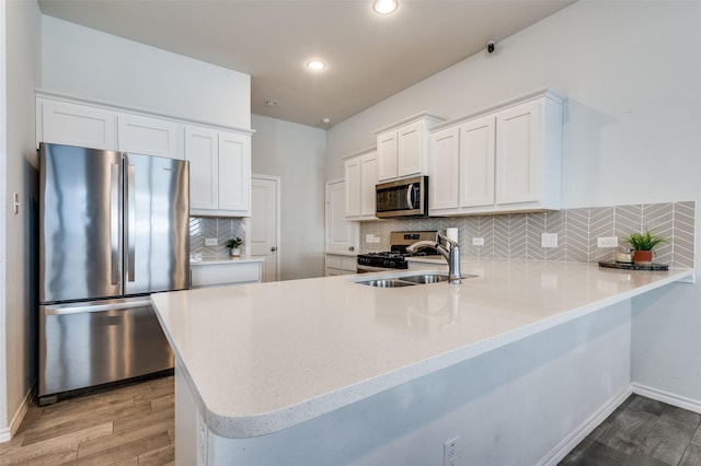 kitchen with a sink, white cabinetry, light wood-style flooring, a peninsula, and appliances with stainless steel finishes