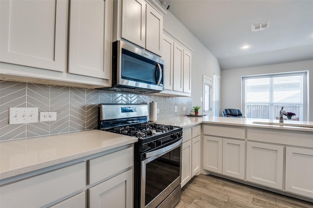 kitchen with stainless steel appliances, light wood-style flooring, a sink, visible vents, and backsplash