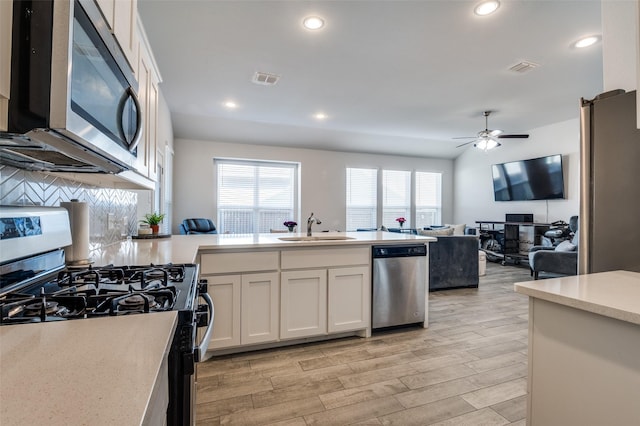 kitchen featuring a peninsula, a sink, ceiling fan, light countertops, and appliances with stainless steel finishes