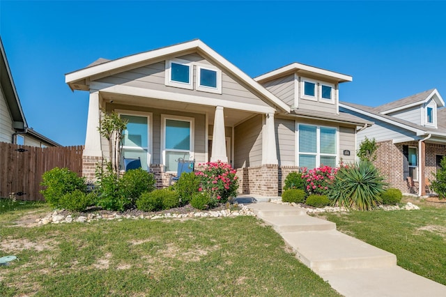 view of front of house featuring fence, covered porch, brick siding, and a front yard