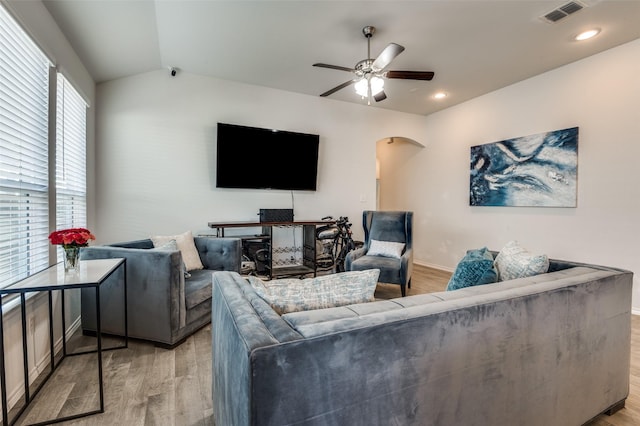 living area featuring vaulted ceiling, visible vents, a ceiling fan, arched walkways, and light wood-type flooring