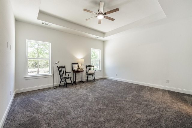 sitting room with ceiling fan, visible vents, baseboards, a tray ceiling, and dark carpet