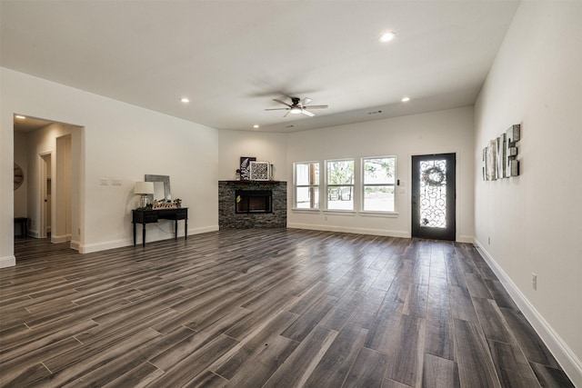 unfurnished living room with a ceiling fan, dark wood-style flooring, a stone fireplace, baseboards, and recessed lighting
