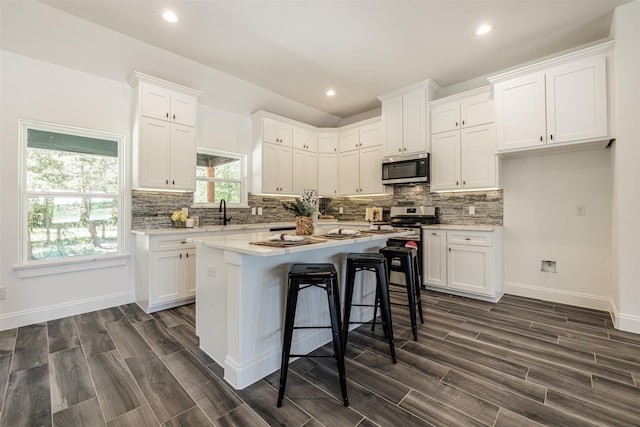 kitchen with wood finish floors, a center island, white cabinetry, stainless steel microwave, and backsplash