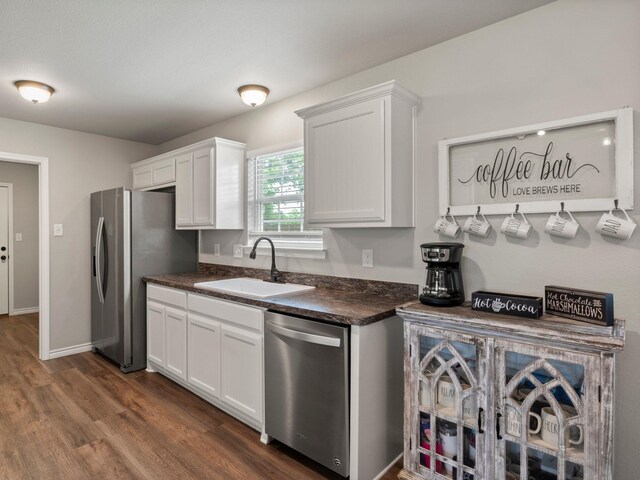 kitchen featuring dark countertops, a sink, white cabinets, dark wood-style floors, and stainless steel appliances