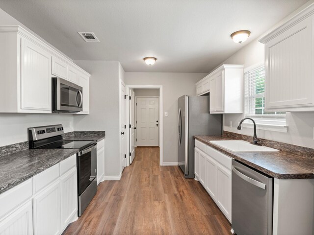 kitchen featuring a sink, stainless steel appliances, white cabinetry, wood finished floors, and visible vents