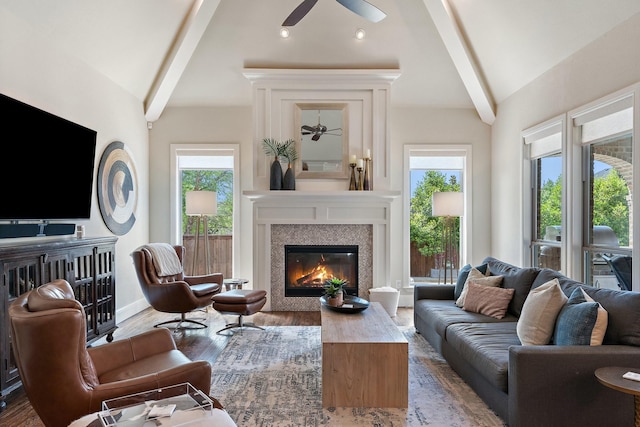 living area with lofted ceiling with beams, a ceiling fan, a glass covered fireplace, and wood finished floors
