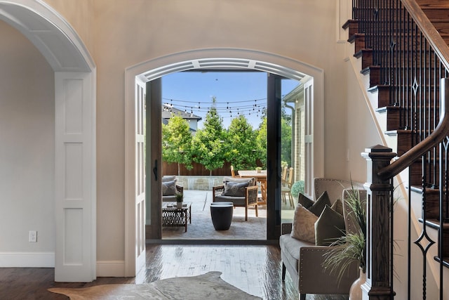 interior space with stairway, arched walkways, wood finished floors, and baseboards