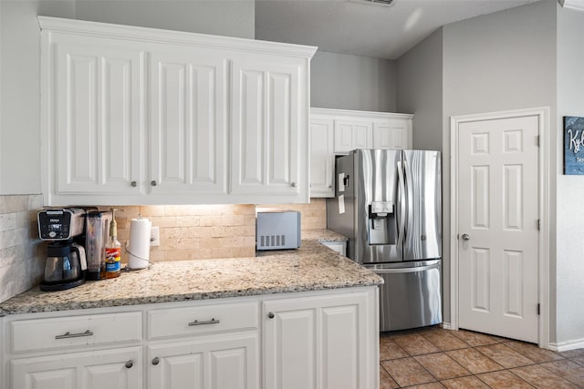 kitchen featuring light tile patterned floors, stainless steel fridge, backsplash, white cabinetry, and light stone countertops