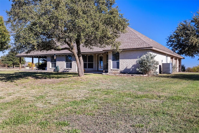 rear view of house with brick siding, a yard, central AC, and a shingled roof