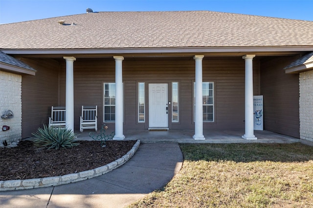 entrance to property featuring roof with shingles, a yard, and a porch