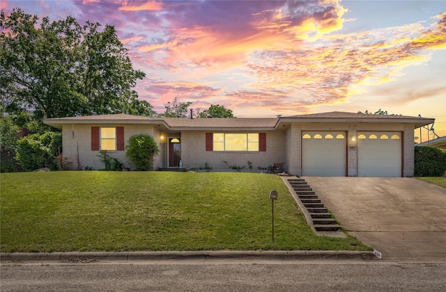 ranch-style home featuring a lawn, an attached garage, brick siding, and driveway