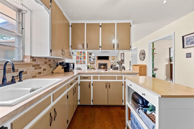 kitchen with dark wood finished floors, light countertops, a fireplace, a sink, and a peninsula