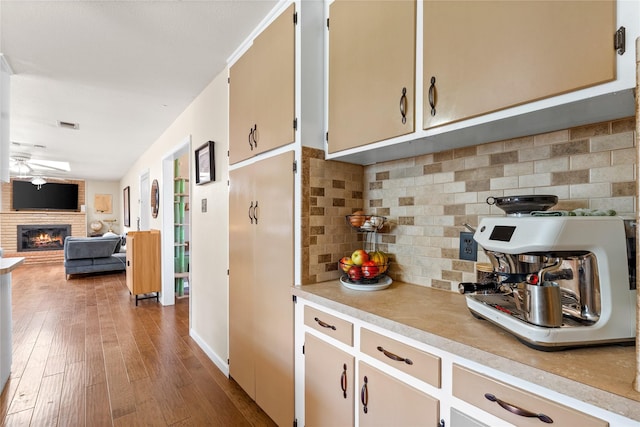 kitchen featuring a ceiling fan, tasteful backsplash, light countertops, a fireplace, and wood-type flooring