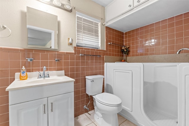 bathroom with tile walls, toilet, vanity, and tile patterned floors